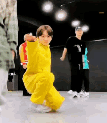 a boy in a yellow jumpsuit is kneeling down in a dance studio .