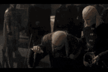 a man with a bald head is kneeling down next to another man with blonde hair .