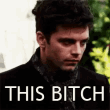 a man in a black suit and scarf is looking at the camera with the words `` this bitch '' written above him .