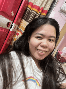a woman in a white shirt with a rainbow on it smiles for the camera