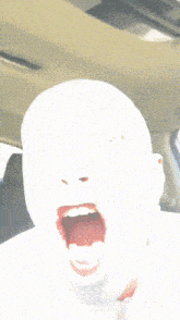 a person with their mouth open in a car with a white face