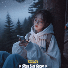 a woman leaning against a tree looking at her phone with situs slot gacor in the corner