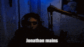 a man wearing headphones stands in front of a shure microphone and says jonathan mains