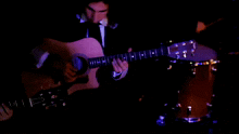 a man in a tuxedo plays a guitar with a purple light behind him