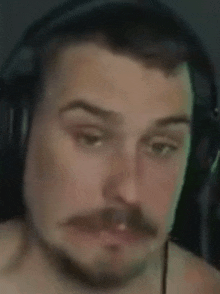 a man with a mustache and headphones on his head is making a funny face .