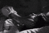 a black and white photo of a woman laying down with her hand on her neck .