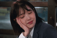 a woman in a suit rests her head on her hand with her eyes closed
