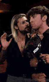 two men are standing next to each other with a microphone that says aew