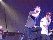 a man singing into a microphone while another man sits on a stage