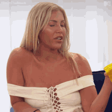 a blonde woman is sitting on a couch holding a yellow cup with the hashtag #exonthebeach on the bottom