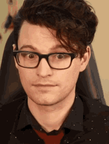 a man wearing glasses and a black shirt looks at the camera