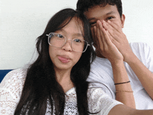 a girl wearing glasses is sticking her tongue out next to a boy covering his face