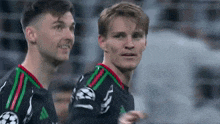 two soccer players are standing next to each other on a field and smiling .