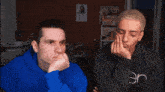 a man in a blue hoodie is talking to another man in a black shirt that says en