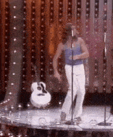 a man is dancing on a stage in front of a microphone while holding a guitar .