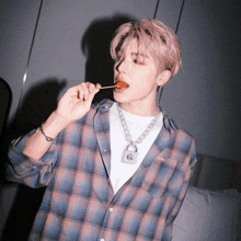 a man wearing a plaid shirt is eating a lollipop with a padlock necklace around his neck