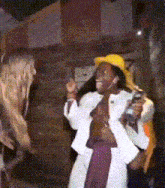 a shirtless man wearing a yellow hat and a white jacket is holding a microphone .