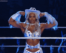 a woman in a white cowboy hat is flexing her muscles in a wrestling ring