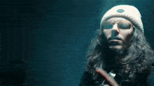 a man with long hair wearing sunglasses and a white hat points to the word my