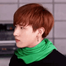 a young man with red hair and a green scarf around his neck is wearing earrings .