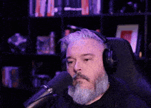 a man with a beard and headphones is talking into a microphone .