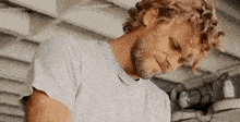 a man with curly hair and a beard is wearing a grey t-shirt and looking down .