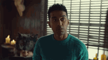 a man in a blue sweater sits in front of a window