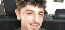 a man with curly hair and a beard is sitting in the back seat of a car .