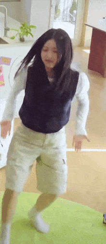 a woman in a vest and shorts is dancing on a green mat .