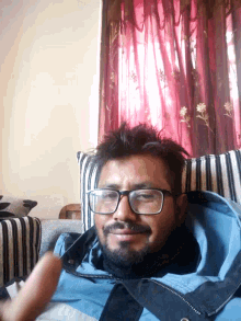 a man wearing glasses and a blue jacket laying on a couch