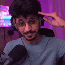 a man with glasses and headphones is sitting in front of a microphone and making a funny face .