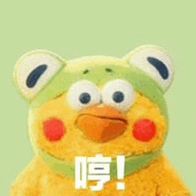 a stuffed animal is wearing a frog hat and making a face .