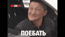 a man sitting in a car with a foreign language on the bottom