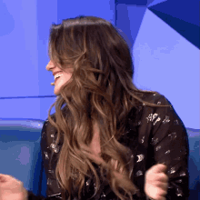 a woman with long hair is sitting on a blue couch laughing