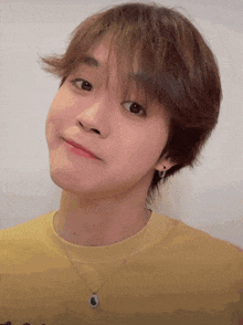 a young man wearing a yellow shirt and a black necklace looks at the camera