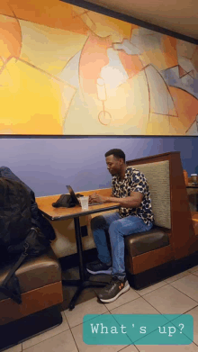 a man sits at a booth in a restaurant using a laptop computer