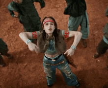a woman with a bandana on her head is standing in the dirt with her arms crossed