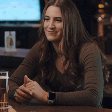 a woman wearing an apple watch sits at a bar with a glass of beer