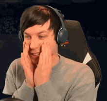 a man wearing headphones is sitting in a chair with his hands on his face and smiling .