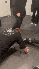 a man wearing a black shirt with a spider on the back crawls on the floor