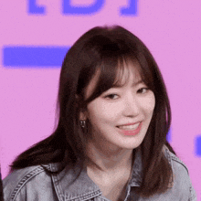 a woman wearing a denim jacket and earrings smiles at the camera