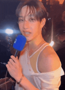 a man wearing a white tank top is holding a blue microphone that says ' nbc ' on it
