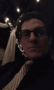 a man wearing glasses and a tie looks at the camera in a dark room