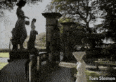 a woman in a white dress stands in front of a gate with the name tom slemen written on the bottom