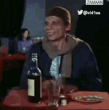 a man is sitting at a table with a bottle of liquor and a glass of beer .