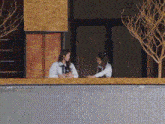 two women are sitting on a balcony looking out a window