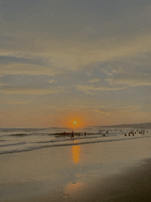 a group of people are walking on a beach as the sun sets behind them