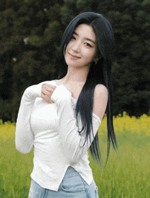 a woman with long black hair wearing a white off the shoulder top and blue jeans