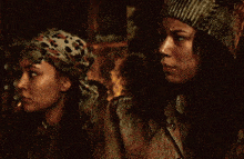 two women are standing next to each other in a dark room . one of the women is wearing a scarf around her head .