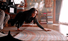 a woman is crawling on a rug in a room with a camera behind her